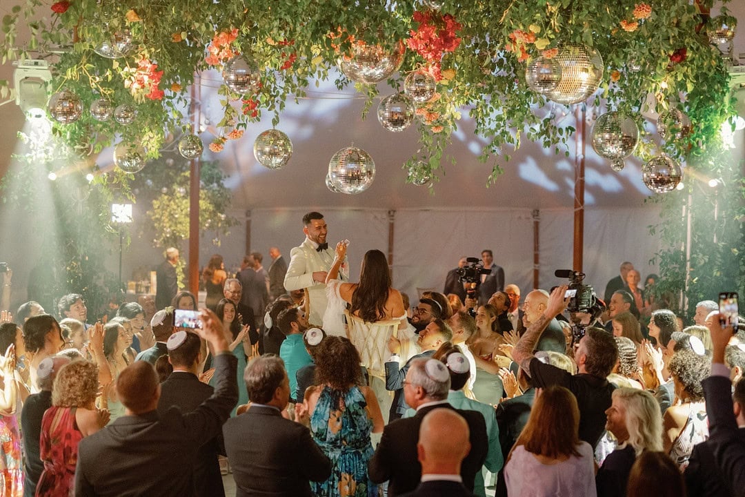Wedding ceremony with bride and groom under floral canopy and hanging decorations.