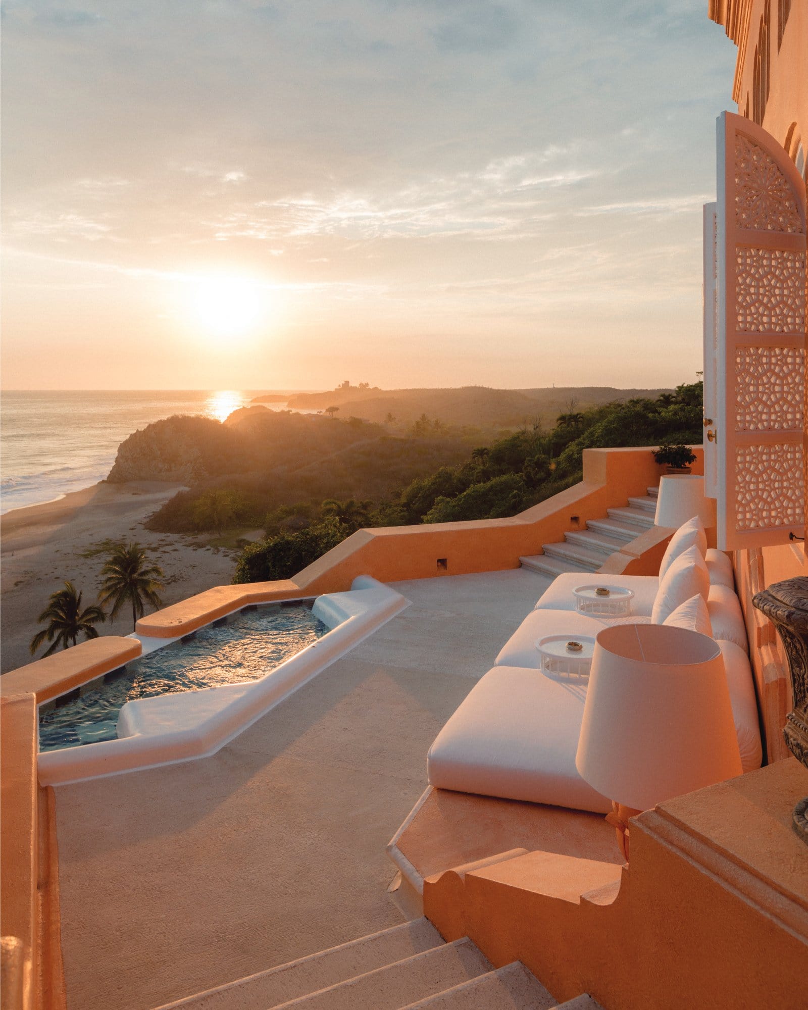 Luxury oceanfront villa with sunset view, pool, and outdoor seating area.