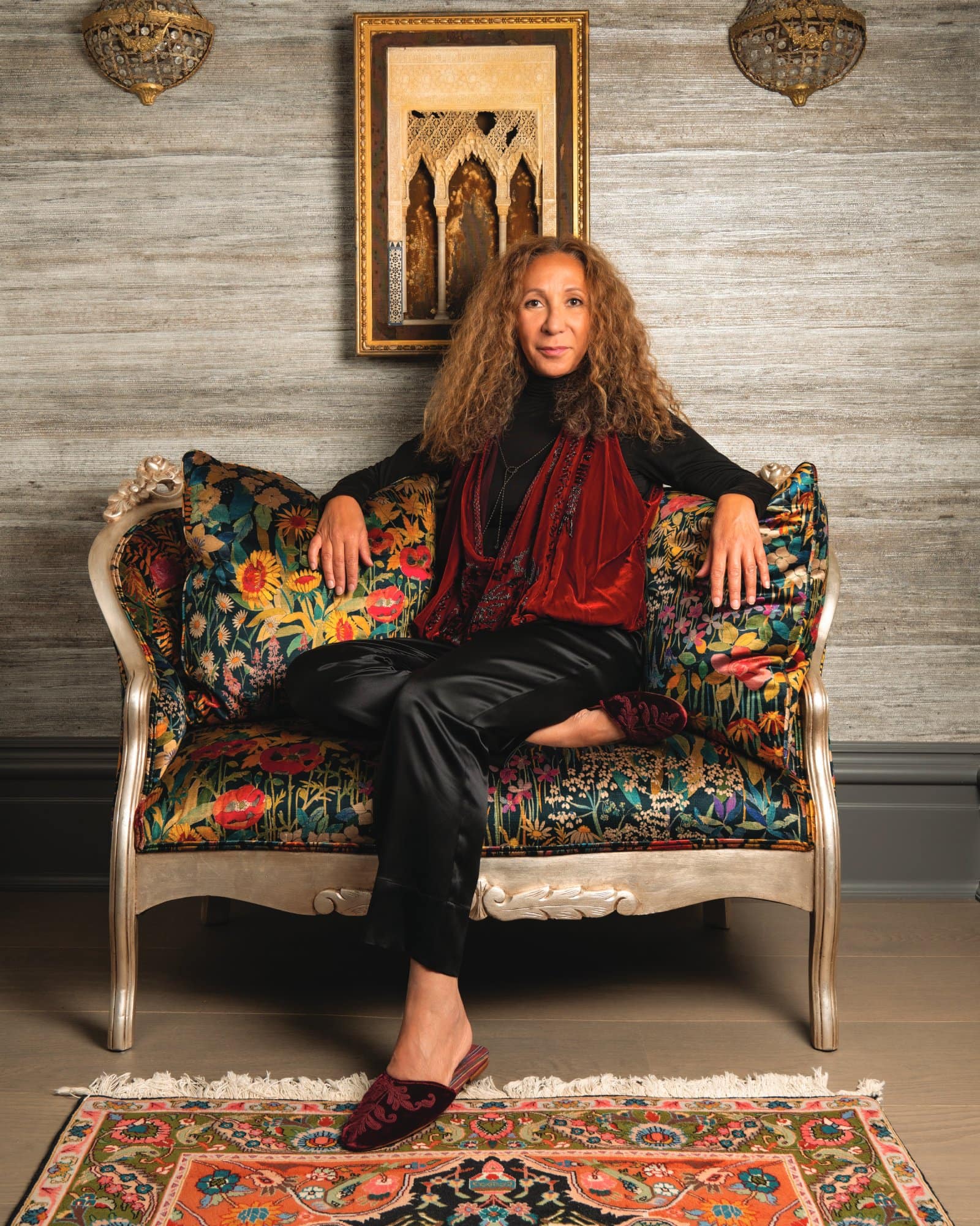 Woman with curly hair sitting on a vintage floral sofa in a stylish room.