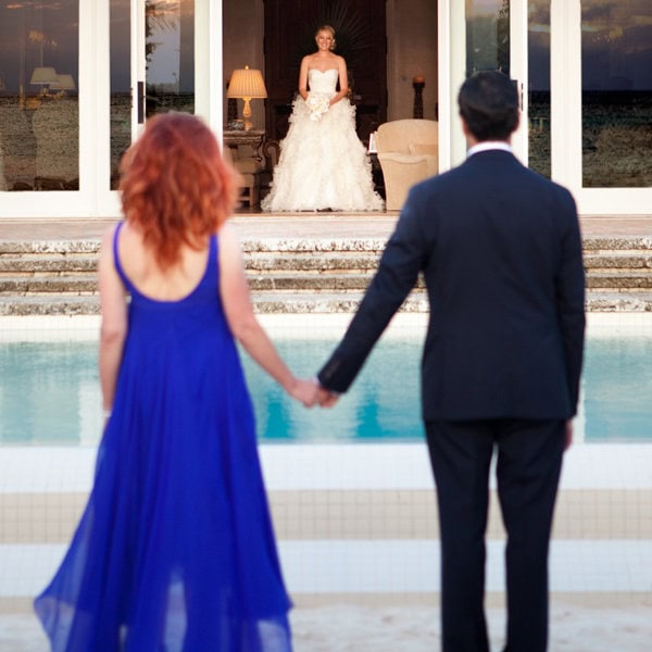 Bride and groom holding hands by the pool with a scenic view.