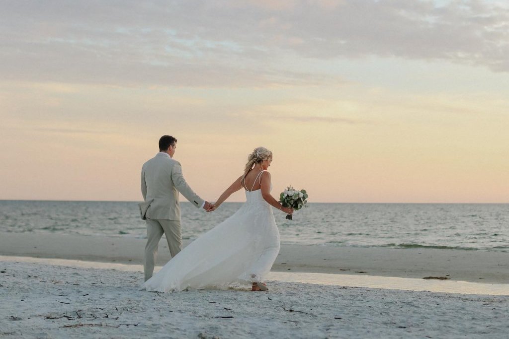 Bride and groom walking on the beach at sunset after wedding ceremony.