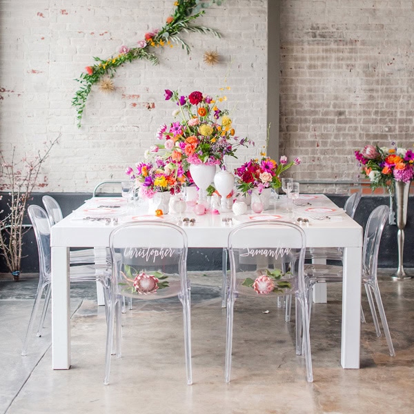 Elegant wedding table setup with colorful floral arrangements and transparent chairs.