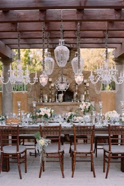 Elegant wedding reception table with chandeliers and floral centerpieces under a wooden ceiling.
