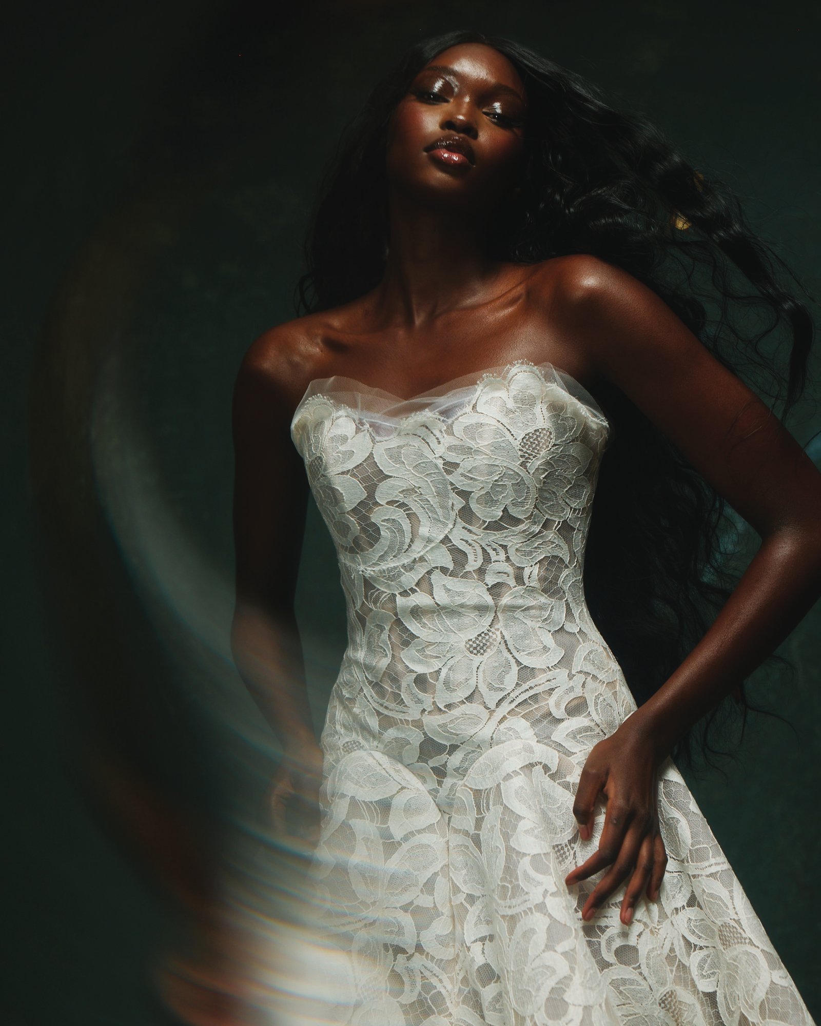 Elegant dark-skinned woman in a white lace wedding dress with flowing hair.